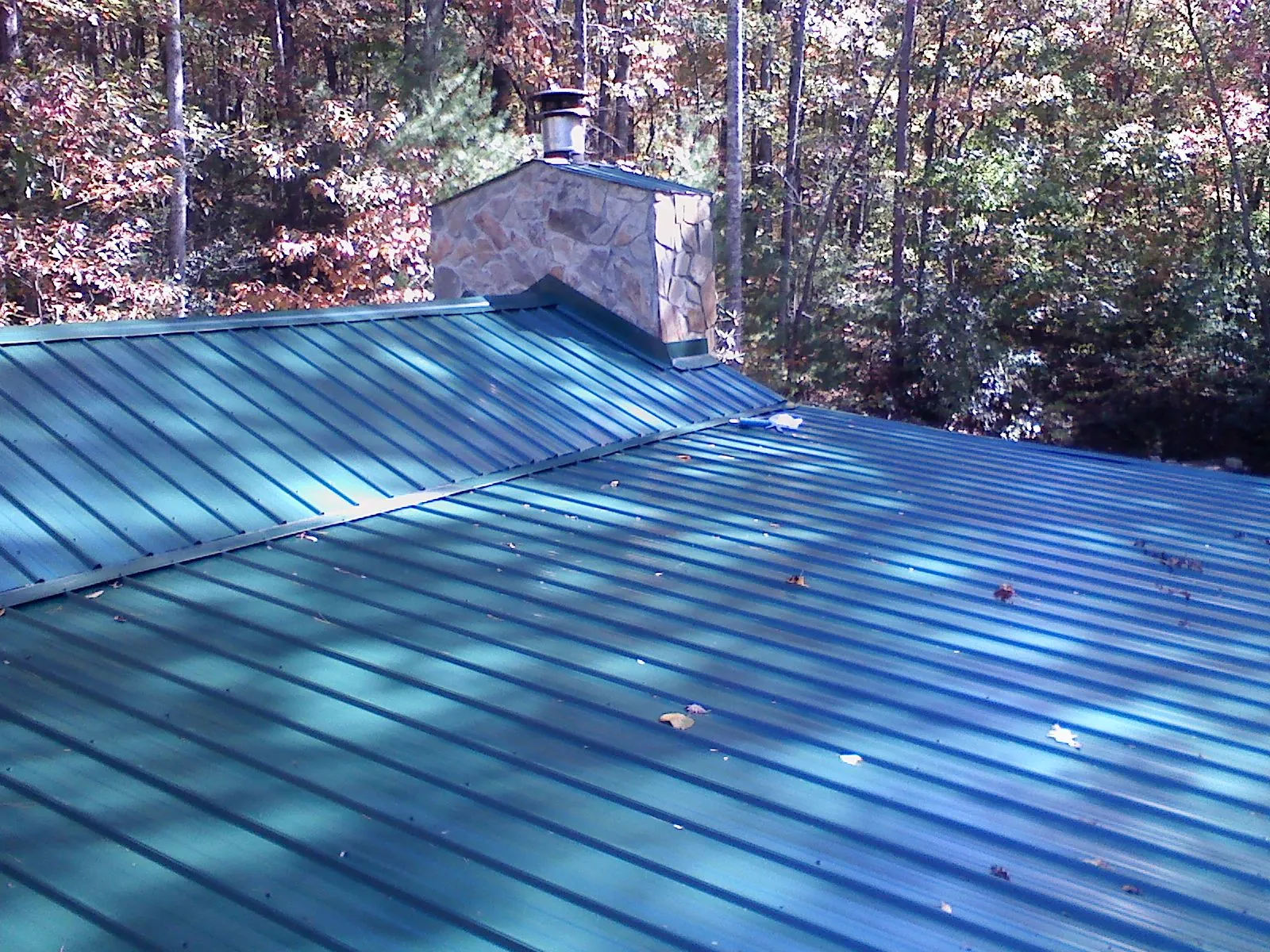 New green metal roof and stone chimney surrounded by autumn woods in Holland